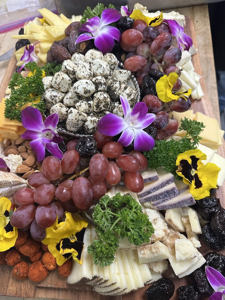 Cheese board with grapes, nuts, dried fruit, herbs, and edible flowers